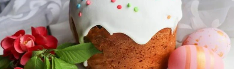 Паска з білою глазур'ю, цукерками та крашанками поруч.