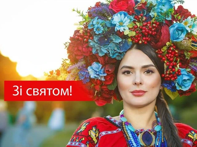 Жінка в українському народному одязі з квітковим вінком на фоні заходу сонця.