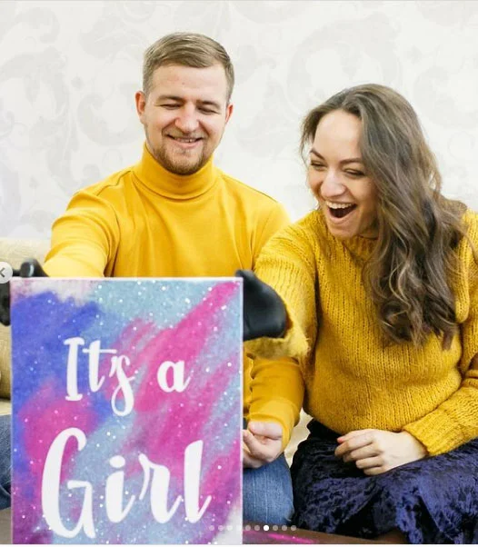 Чоловік і жінка тримають табличку з написом It's a Girl на фоні галактики.